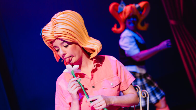 Actrice met blonde pruik likt aan een bloem.