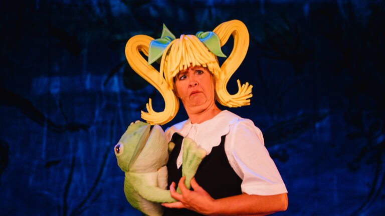 Actrice met blonde pruik heeft een kikken in haar armen.