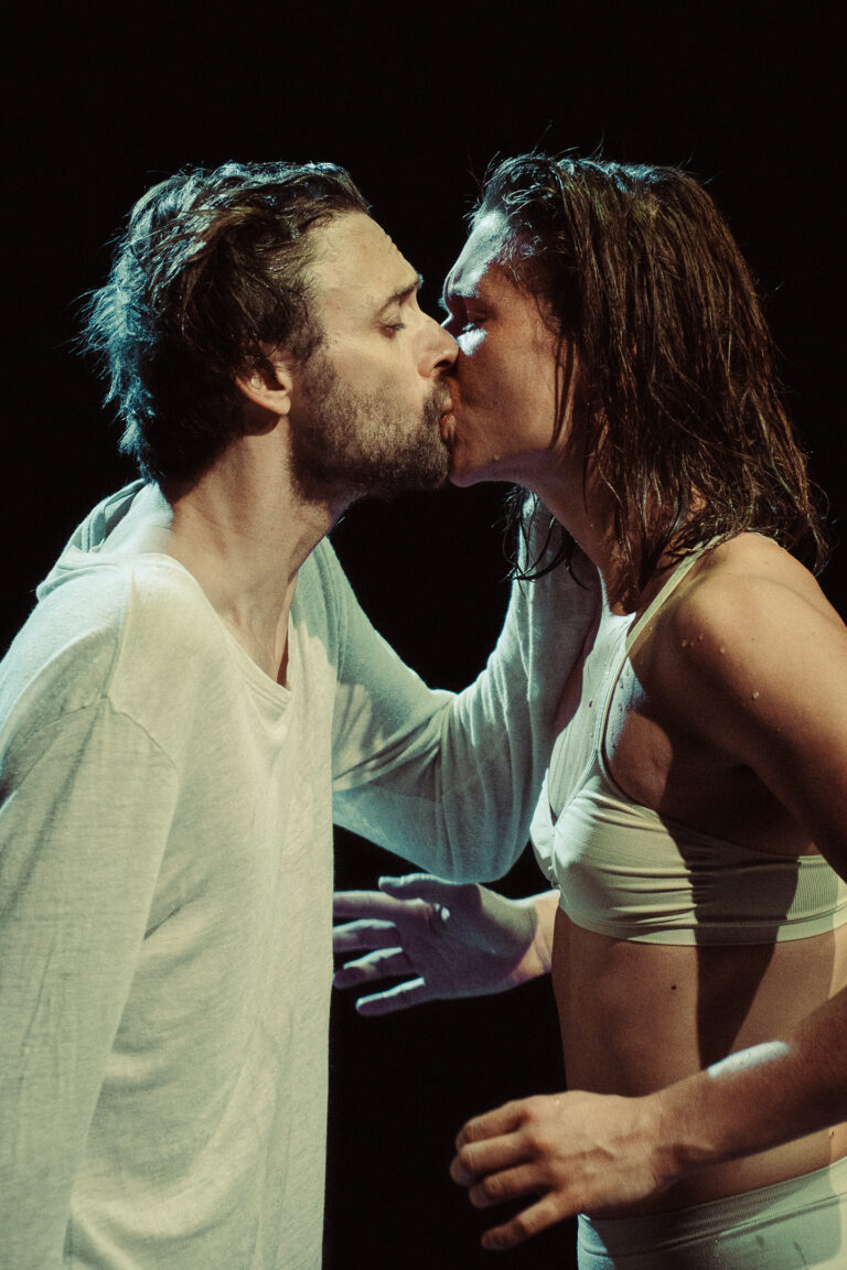 Twee mensen staan dicht bij elkaar en kussen elkaar op het podium.