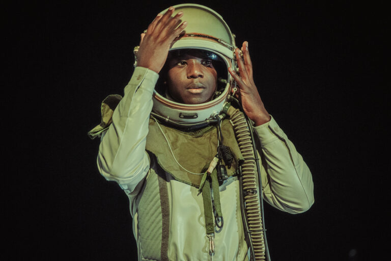 Een persoon trekt een ruimtehelm aan, gekleed in een astronautenoutfit.