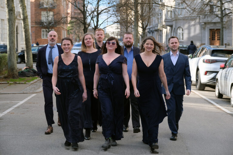 Acht netjes geklede mannen en vrouwen die lachend richting de camera lopen.