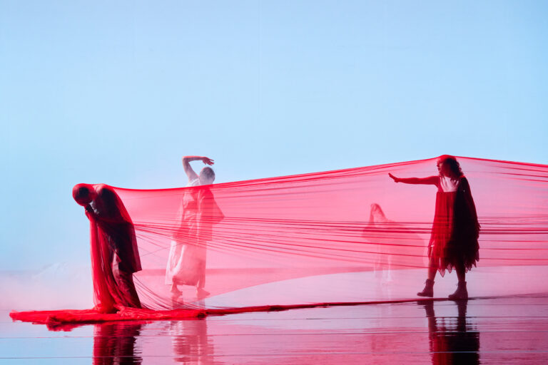Scènefoto twee mensen met rood doek en persoon achter het doek