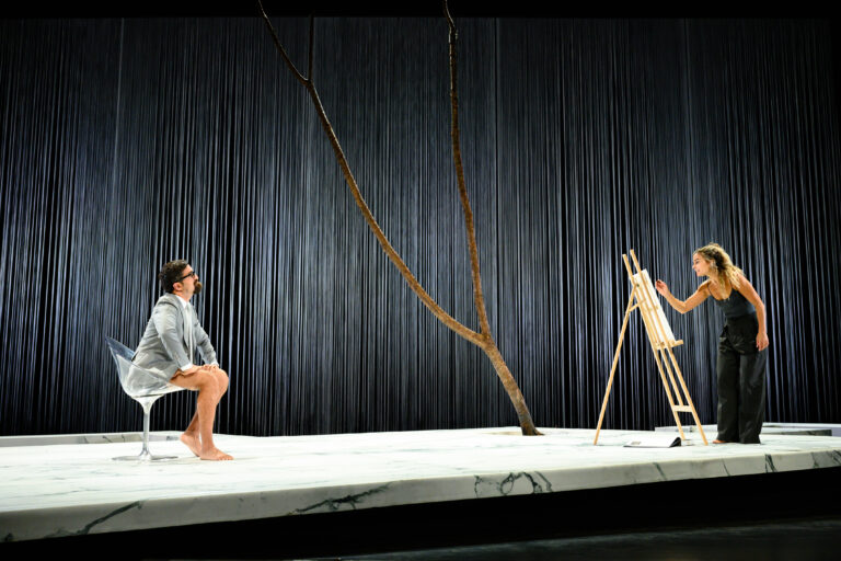 Een kunstenaar schildert een model dat op een stoel zit, terwijl een tak een belangrijk visueel element in de scène vormt.