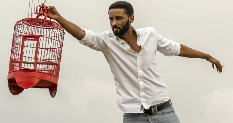 Fuad Hassen in wit overhemd spreidt armen met rode vogelkooi
