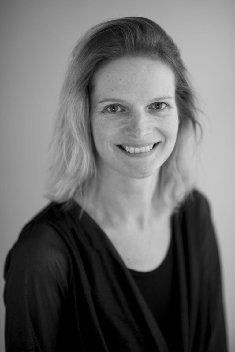 Portret van een vrouw met een glimlach, gekleed in een zwarte top, tegen een neutrale achtergrond.
