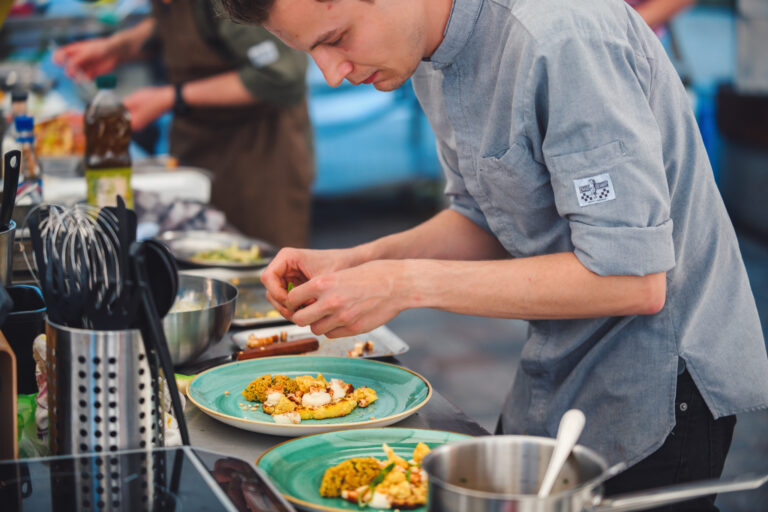 Een chef-kok bereid een gerecht op een groen bord in een professionele keukenomgeving.