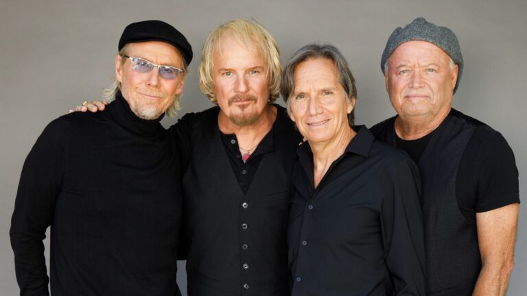 Vier mannen 60-plus zwart gekleed met grijze achtergrond.