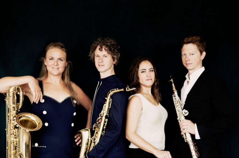 Een groep van vier muzikanten poseert voor een zwarte achtergrond, elk met een muziekinstrument.