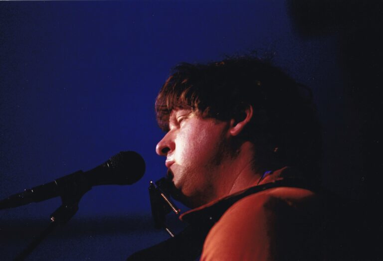 Een muzikant die een gitaar speelt en zingt, gefotografeerd in een blauwe verlichting.