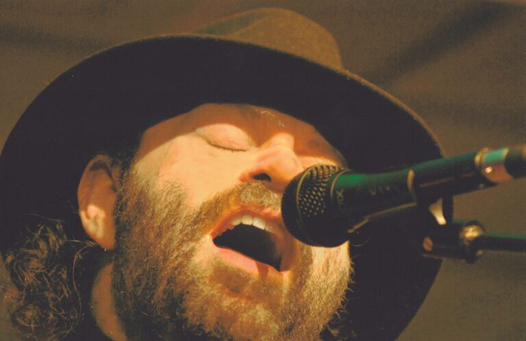 Een zanger met een hoed die intens in de microfoon zingt.