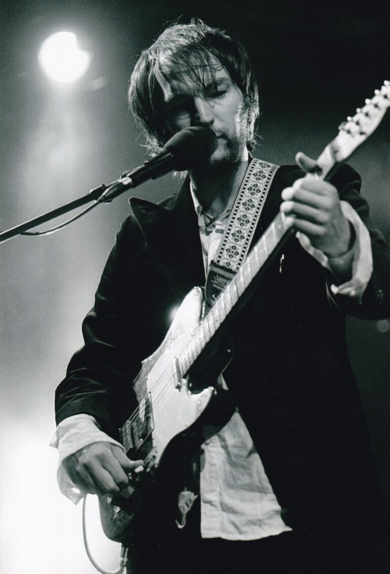 Een muzikant speelt gitaar en zingt in een donkere concertsetting.