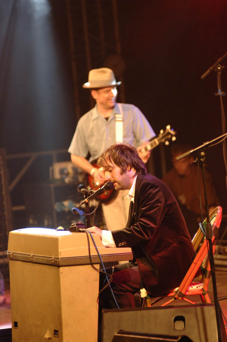 Twee muzikanten optreden op een podium, waarbij één op een keyboard speelt en de ander gitaar speelt.