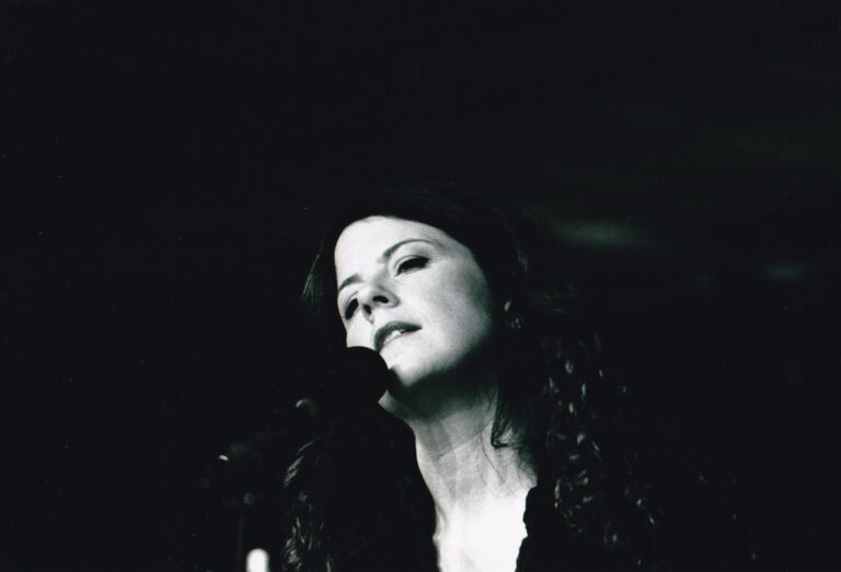 Zwart-witfoto van een vrouwelijke zangeres die emotioneel naar het publiek kijkt terwijl ze in een microfoon zingt.