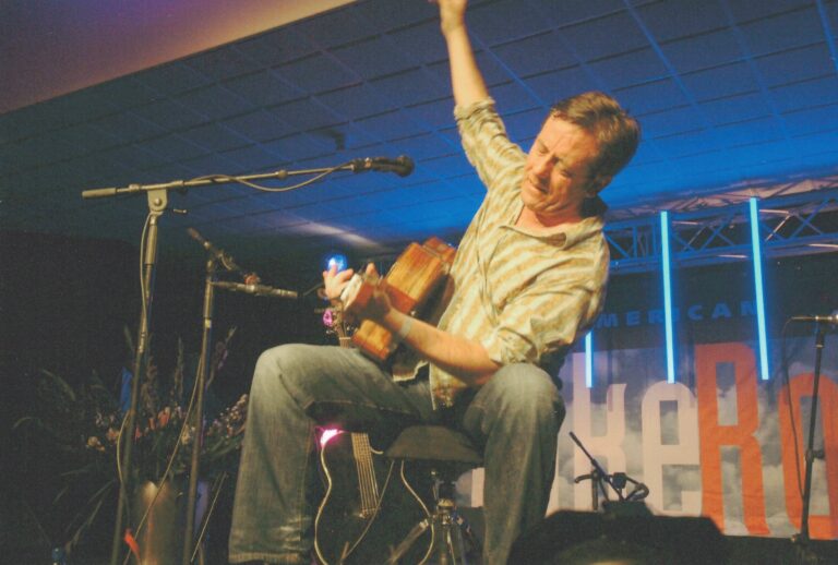 Een muzikant speelt enthousiast gitaar op een podium met blauwe verlichting.