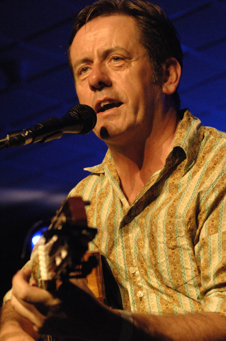 Een man zingt en speelt gitaar tijdens een live optreden.