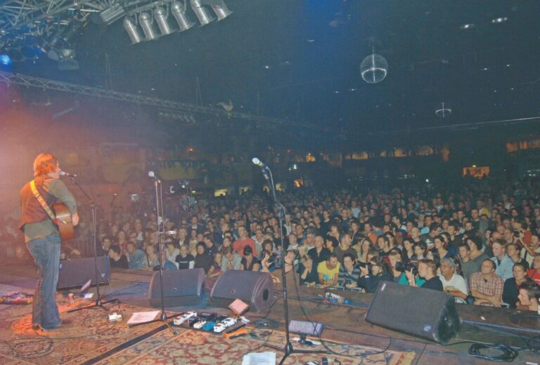 Een druk bezochte concertzaal met een groot publiek en muziekinstrumenten op de voorgrond.