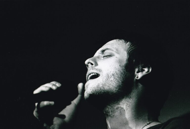 Zwart-wit afbeelding van een man die intensief zingt met een focus op zijn gezichtsuitdrukking.