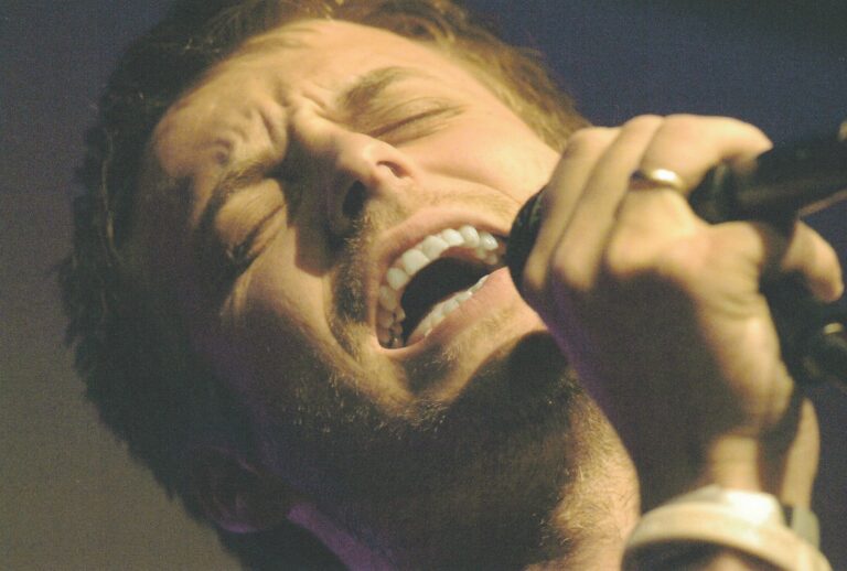 Een zanger die intens in de microfoon zingt met een geconcentreerde uitdrukking op zijn gezicht.