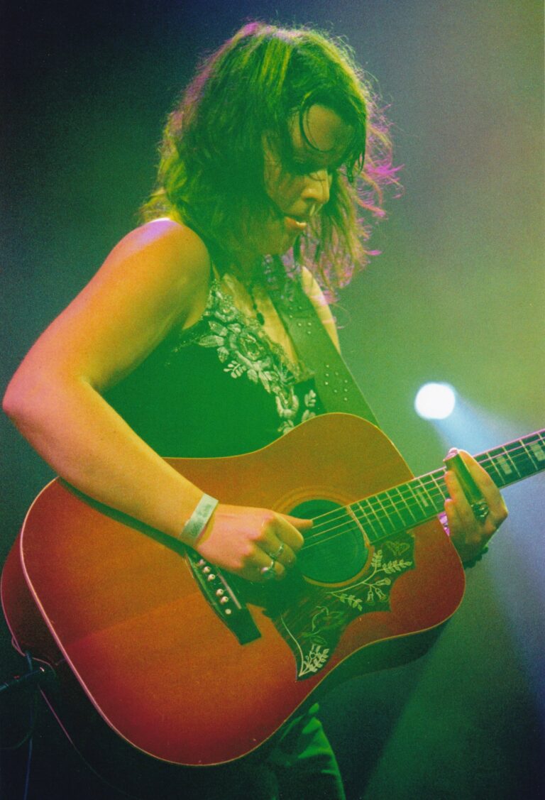 Een muzikante speelt gitaar op een podium, omringd door sfeervolle verlichting.