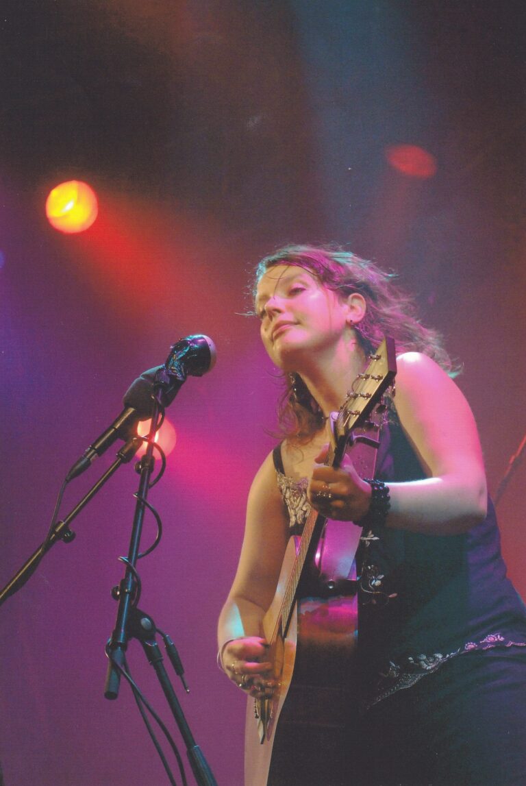 Een muzikante speelt gitaar op een podium met kleurrijke verlichting.
