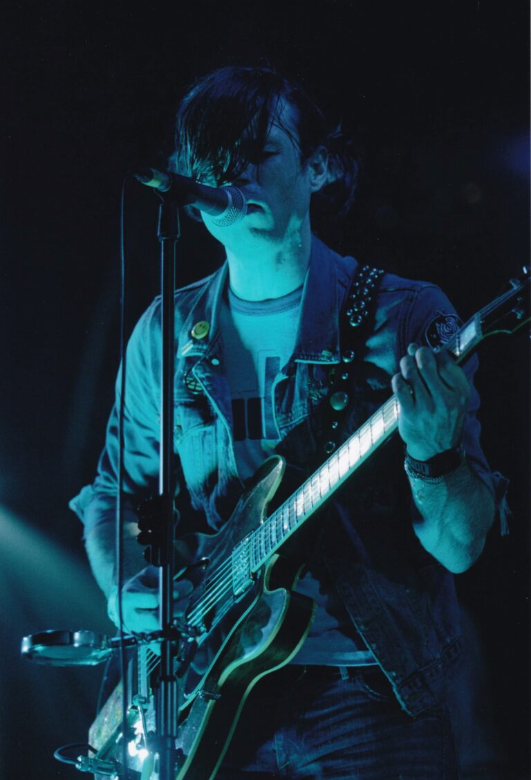 Een muzikant speelt gitaar en zingt op een podium, omgeven door blauwe verlichting.