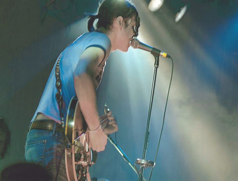 Een muzikant op het podium met een gitaar, zingend in een lichtgevende omgeving.