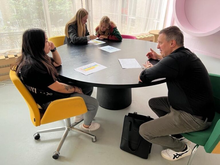 Een vergadering met vier mensen rond een grote tafel in een moderne ruimte.