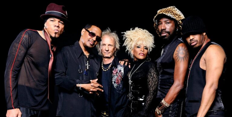 Een afbeelding met alle 6 de bandleden van Mother's Finest in zwarte kleding voor een zwarte achtergrond.