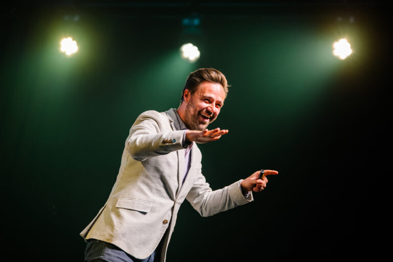 Lammert Kamphuis wijst met twee handen en lacht in de camera