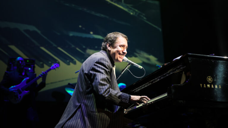 Foto van Jools Holland achter de piano, hij kijkt naar rechts en lacht.