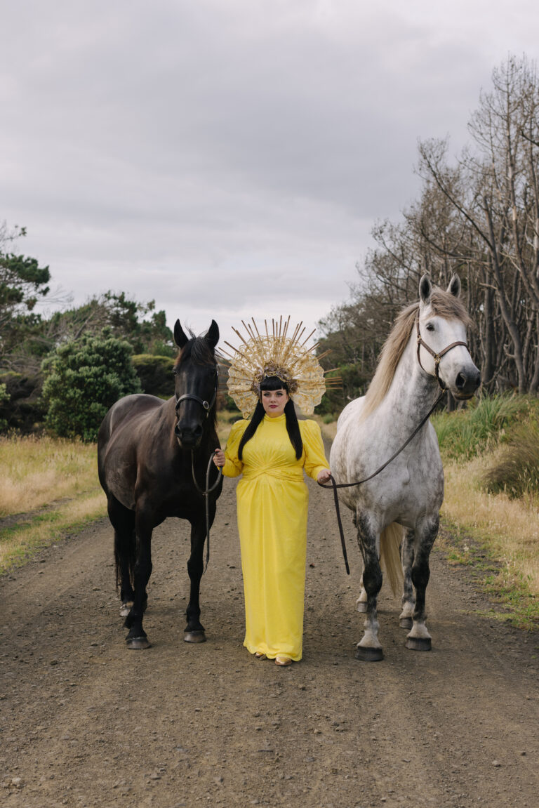 Een afbeelding van Tami Neilson in een gele jurk met twee paarden aan haar zijde.