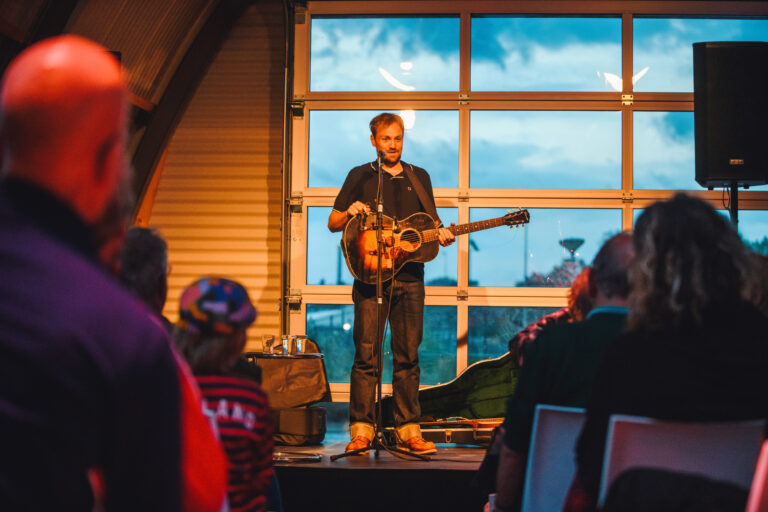 Tim Knol op podium in informatiecentrum nieuwe Stationsgebied met een aantal mensen in publiek op voorgrond.