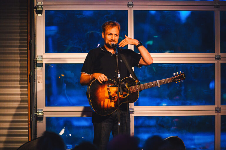 Tim Knol met gitaar op podium in informatiecentrum