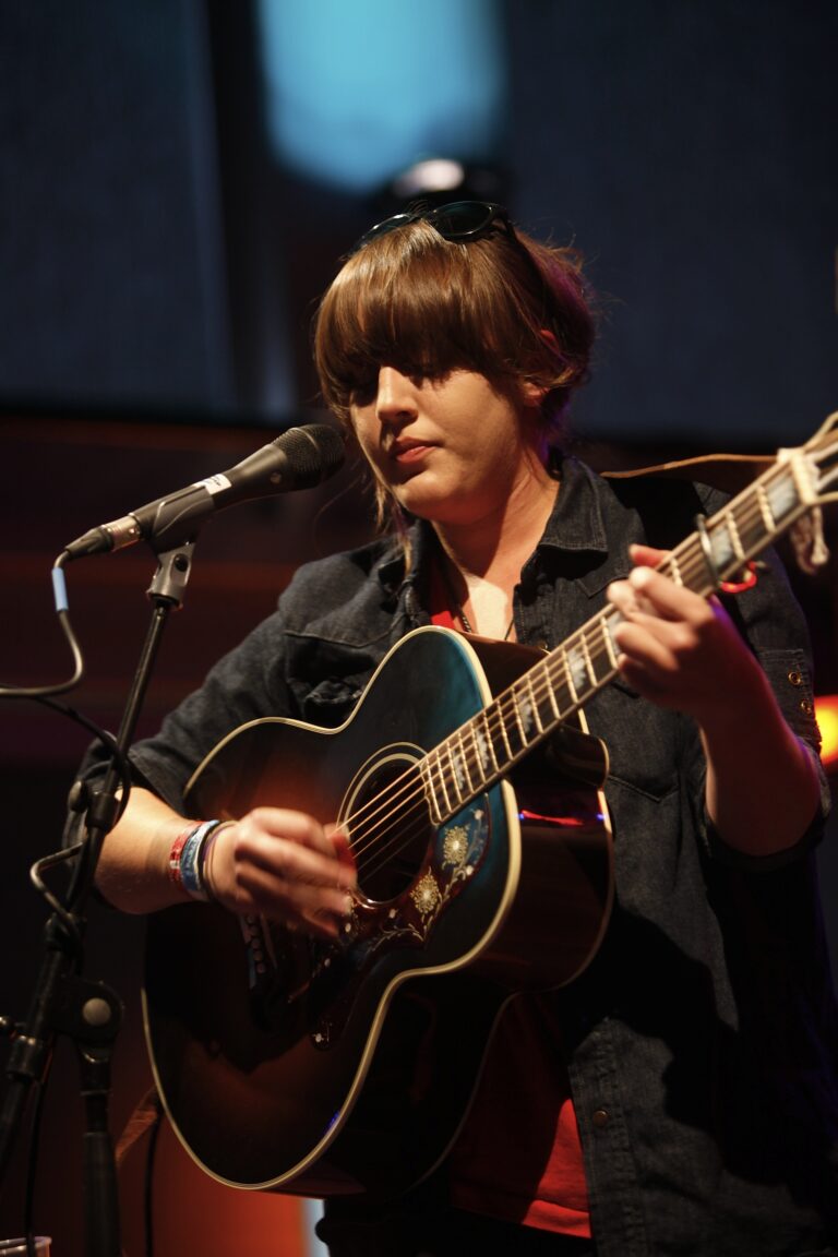 Een muzikante speelt met een gitaar terwijl ze zingt in een intieme setting.