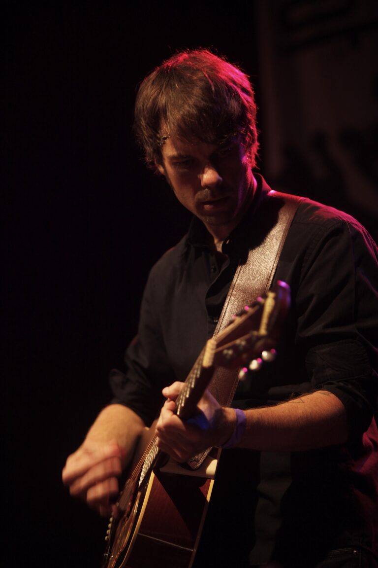 Een muzikant speelt gitaar onder gedempt licht op het podium.