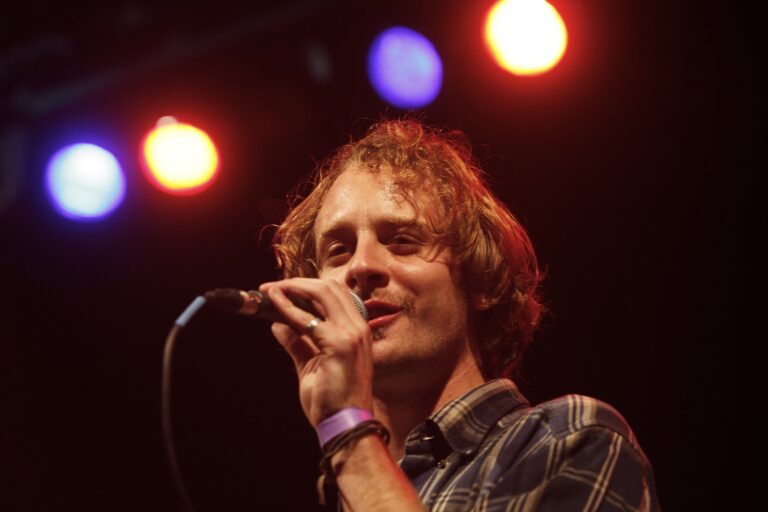 Een zanger die op het podium microphone vasthoudt met kleurenrijke lichten op de achtergrond.