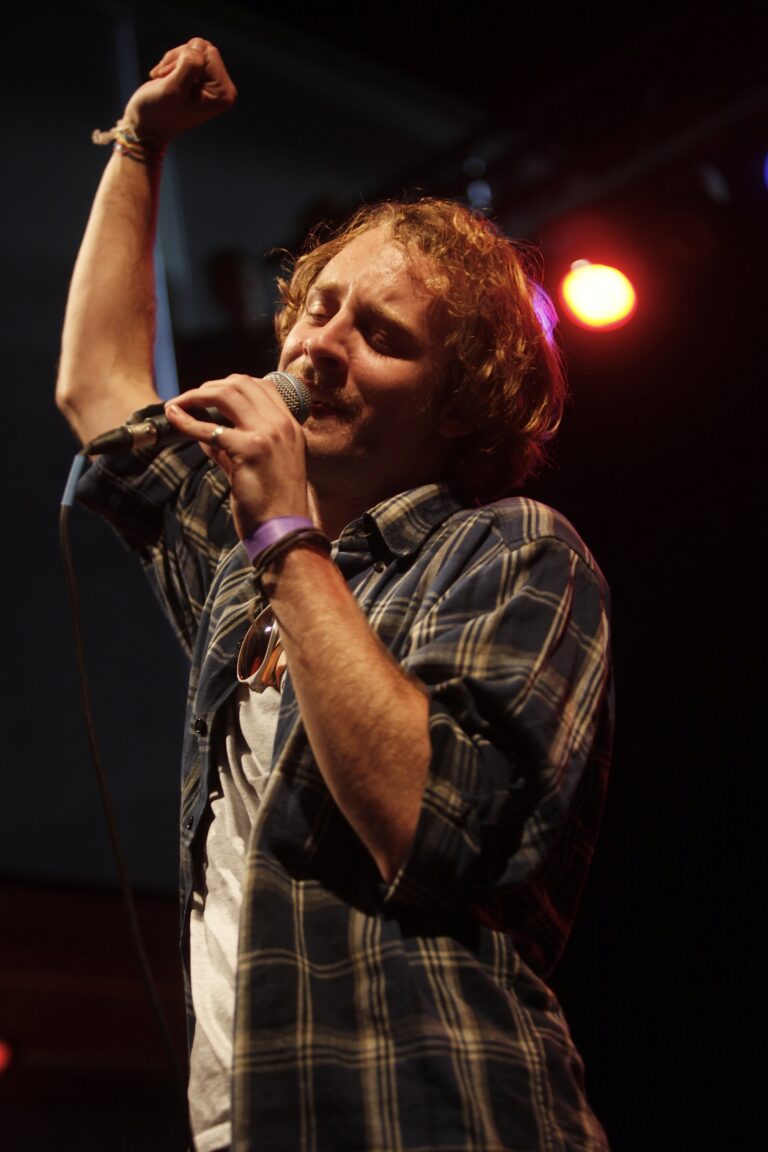 Een zanger voert een optreden uit met een microfoon in de hand, terwijl hij emotioneel lijkt te genieten van de muziek.