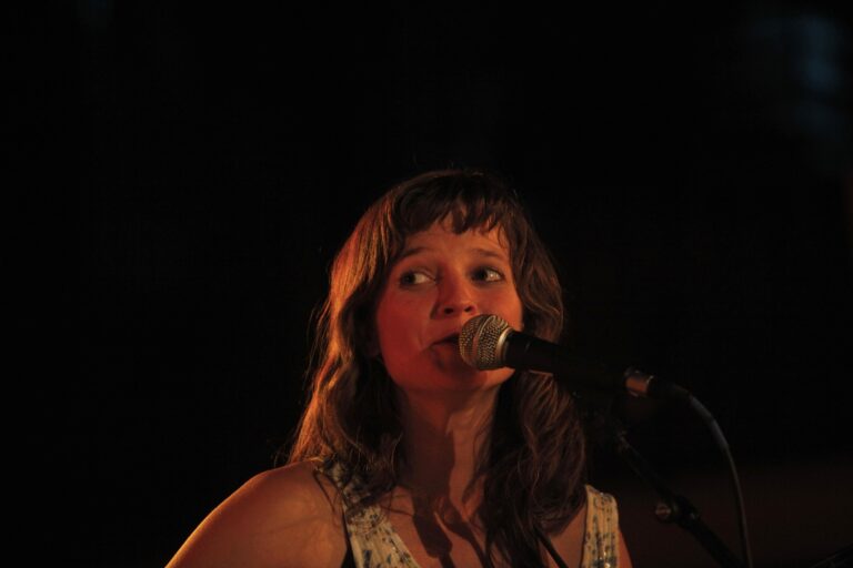 Een vrouw met bruin haar zingt in een microfoon onder gedimde verlichting.