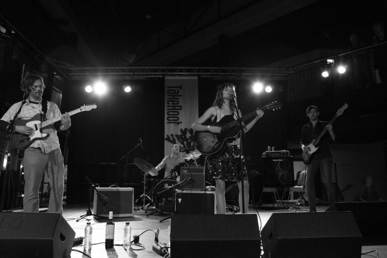Een band speelt live op een podium met verschillende instrumenten en verlichting.