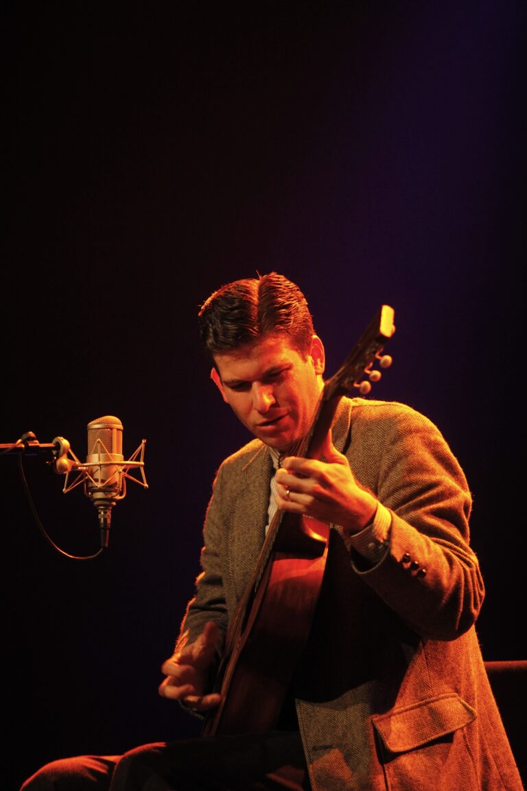 Een muzikant speelt gitaar op het podium, met een microfoon in de buurt en een sfeervolle verlichting.