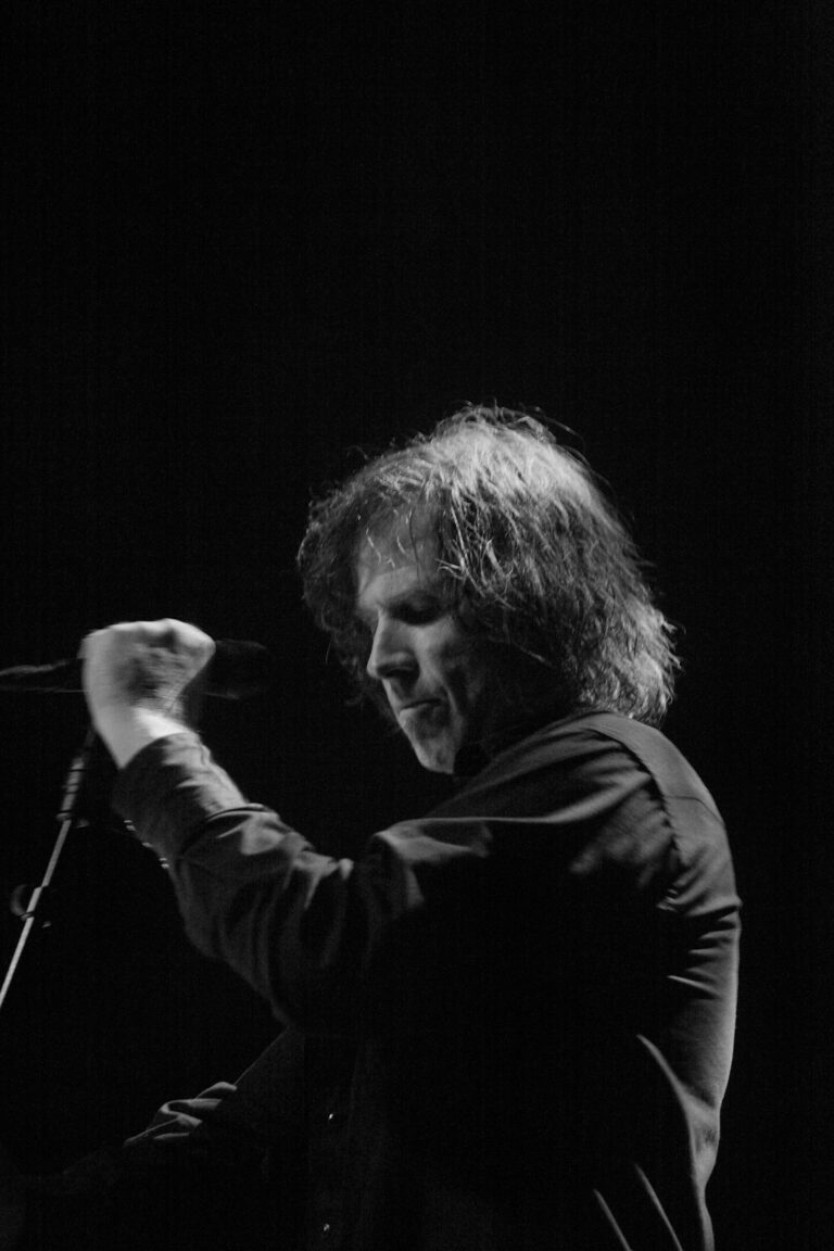 Een muzikant in zwart-wit die intensief in de microfoon kijkt en met de hand een gebaar maakt.