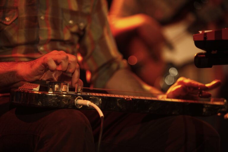 Close-up of a musician’s hand playing a slide guitar on stage.