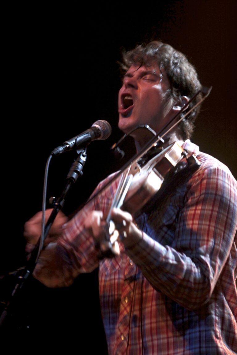 Een muzikant op het podium zingt en speelt viool in een energieke optreden.