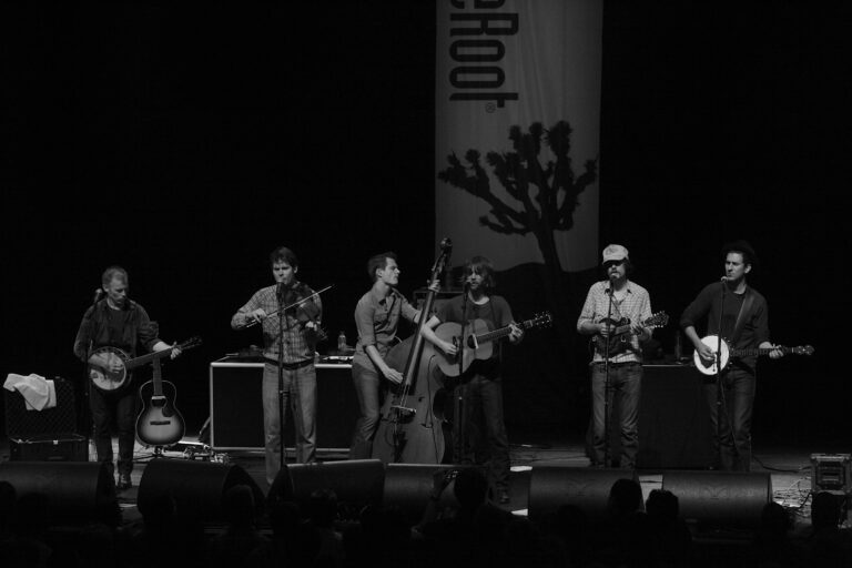 Een band speelt live op het podium met verschillende instrumenten in een zwart-wit afbeelding.