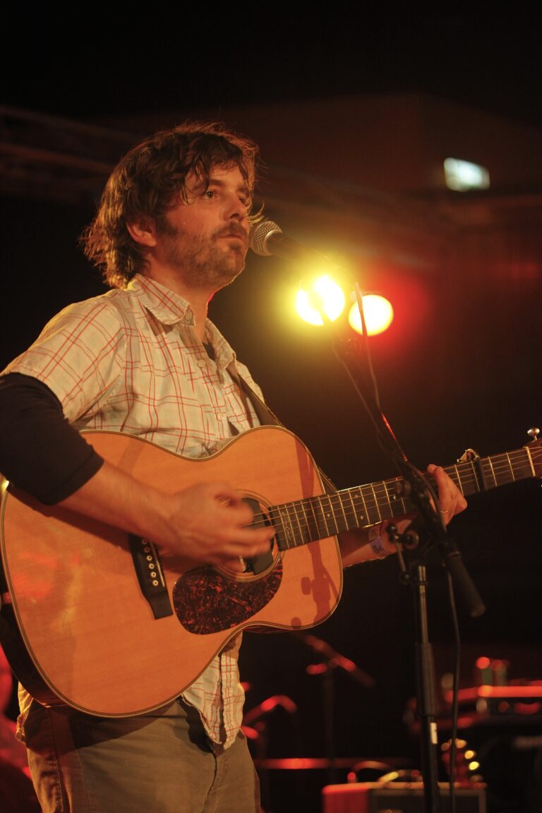 Een muzikant speelt gitaar en zingt op een podium met warme verlichting.
