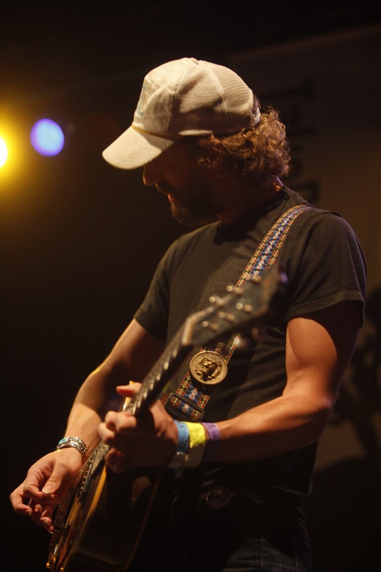 Een muzikant speelt gitaar op een podium met warm gekleurde lichten.