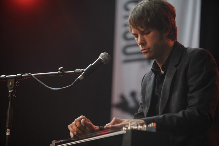 Een muzikant speelt op een keyboard met een microfoon in de buurt, terwijl hij geconcentreerd naar zijn instrument kijkt.