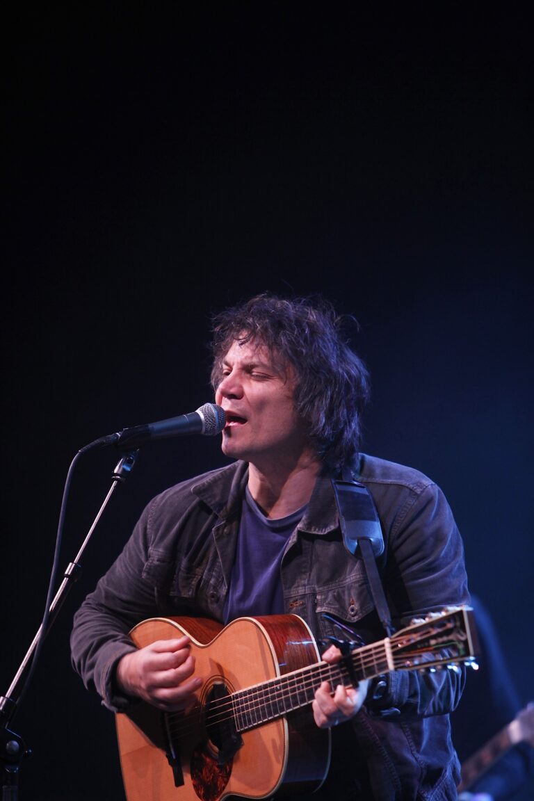 Een muzikant zingt en speelt gitaar op het podium met een donkeren achtergrond.