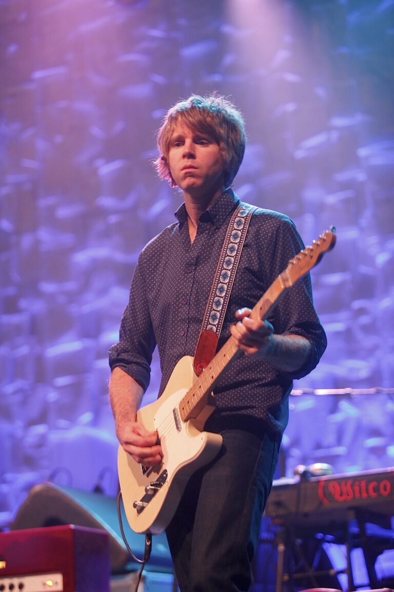 Een muzikant staat op het podium en speelt gitaar met een kleurrijke achtergrond.