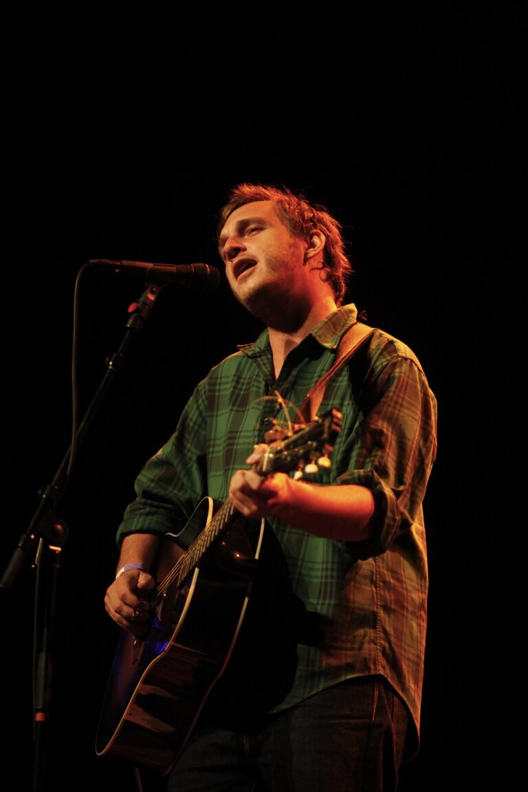 Een muzikant zingt en speelt gitaar op het podium met een microfoon.
